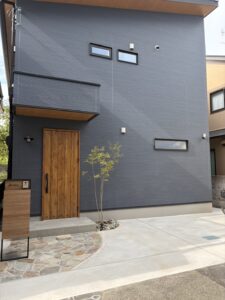ネイビーの外観に天然石とブラウンを合わせたナチュラルモダンな外構
